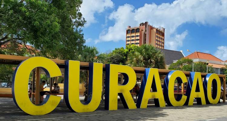 Large yellow CURACAO letters in a plaza with trees and blue sky.