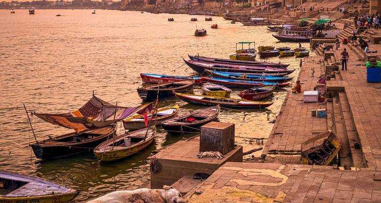 Tientallen houten boten afgemeerd langs de trappen van de Ganges rivier met mensen die ontspannen bij zonsondergang
