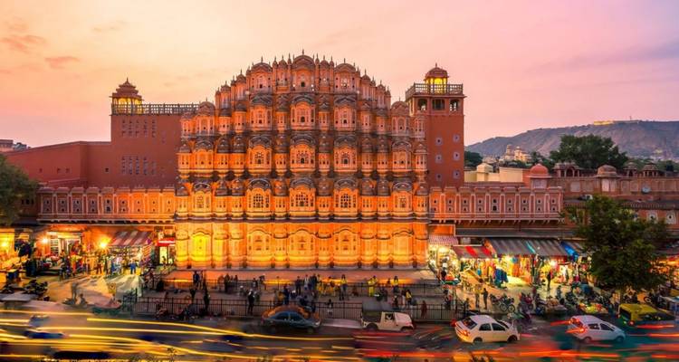 Hawa Mahal verlicht bij schemering met drukke straatverkeerstrepen op de voorgrond en roze lucht