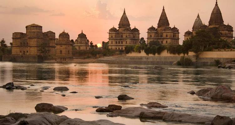 Silhouettierte Kenotaphe von Orchha spiegeln sich im ruhigen Fluss bei pastellfarbenem Sonnenuntergang wider