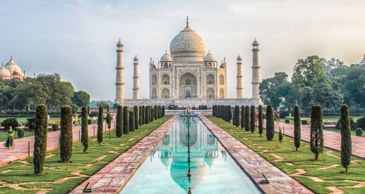Klassischer Postkartenblick auf das Taj Mahal mit Wasserbecken und zypressengesäumten Gärten im sanften Morgenlicht