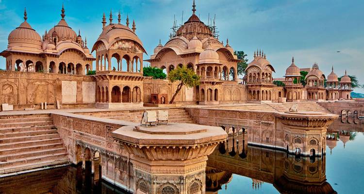 Elegante Sandstein-Kenotaphe mit verzierten Kuppeln, die sich in einem stillen Wasserbecken unter einem klaren blauen Himmel spiegeln