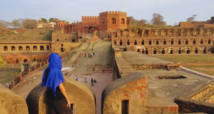 Ein Reisender in einem blauen Kopftuch blickt über die Wallmauern einer weitläufigen roten Sandstein-Festungsanlage