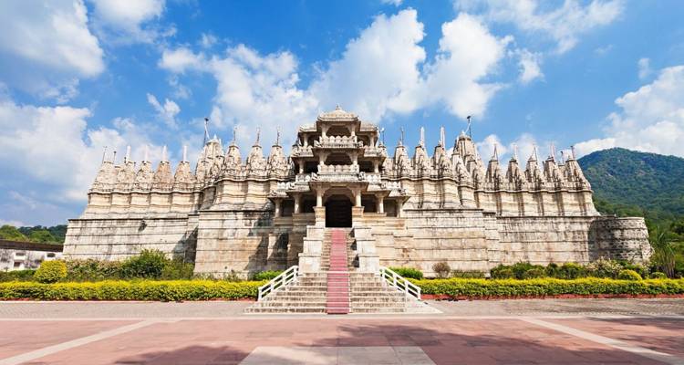 Symmetrische marmeren Jain-tempel met sierlijke torens omlijst door blauwe lucht en weelderig groen