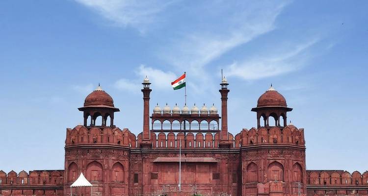 Red Fort with Indian flag flying high against bright blue sky.