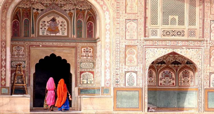 Drie vrouwen in felgekleurde sari's lopen door een sierlijke Mogol-tijdperk boogvormige deuropening met ingewikkelde bloemenfrescos