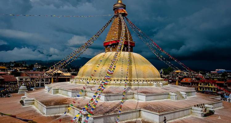 Levendige gebedsvlaggen bedekken de gouden koepel van Boudhanath Stupa onder dramatische moesonwolken