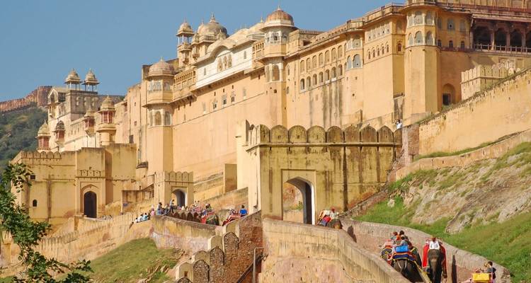 Rij toeristen die op olifanten de helling oprijden naar de torenhoge muren van Amber Fort