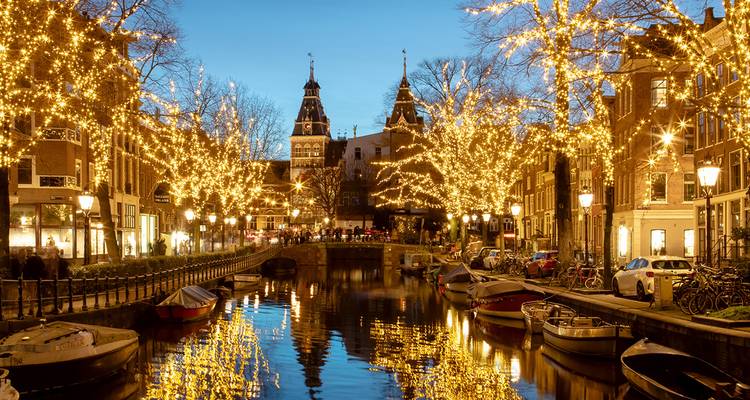 Canal de Ámsterdam reluciendo con luces festivas que se reflejan en el agua durante la hora azul.