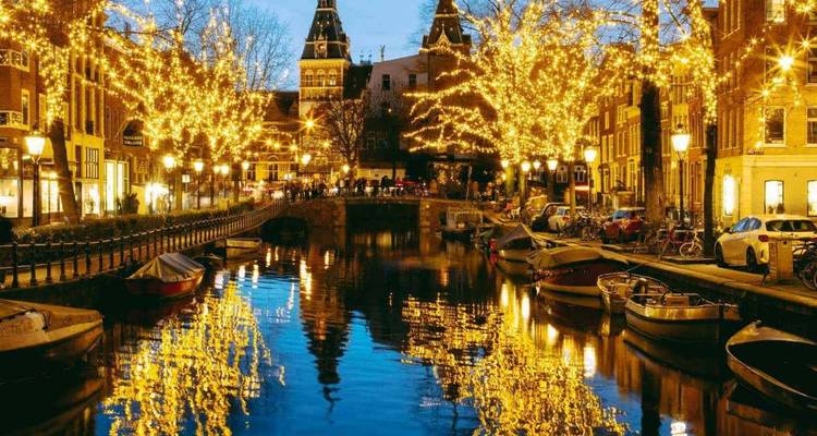 Les canaux d'Amsterdam brillent de lumières dorées festives se reflétant dans l'eau sous un ciel crépusculaire.