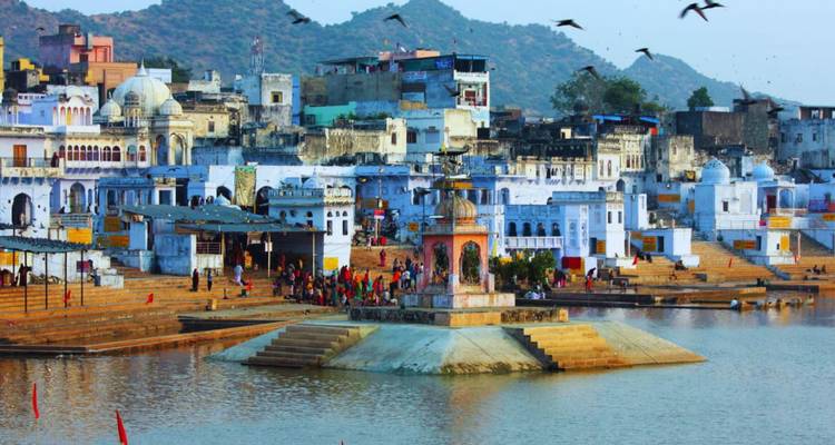 Ghats colorés et temples entourant le lac sacré de Pushkar avec des oiseaux volant au-dessus