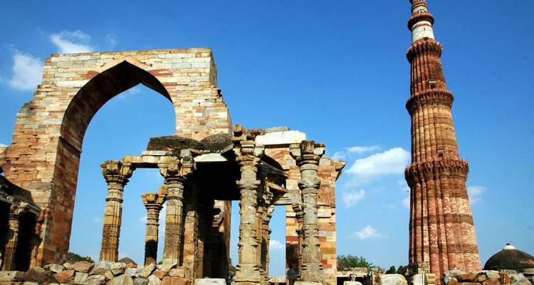 Towering Qutub Minar rises beside ancient stone arches under a bright blue sky