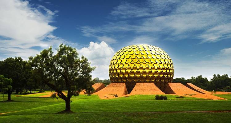 Une grande structure sphérique dorée (Matrimandir) posée sur des supports en grès rouge au milieu d'une pelouse verte entretenue sous un ciel bleu avec des nuages épars.