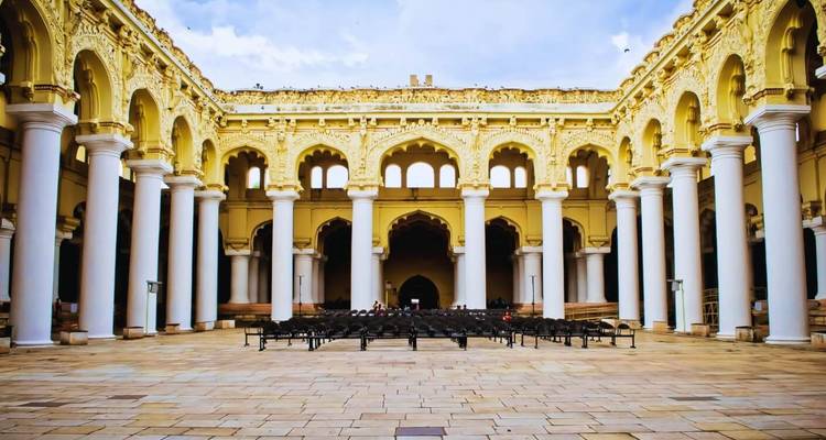 Cour symétrique du palais Thirumalai Nayakkar avec de hautes colonnes blanches et des arches jaunes ornementées sous un ciel dégagé.