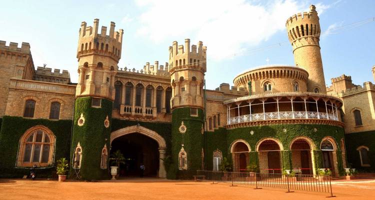 Großartiger efeuumrankter Bangalore-Palast mit Türmchen, Bögen und einer runden Veranda unter hellem Himmel.