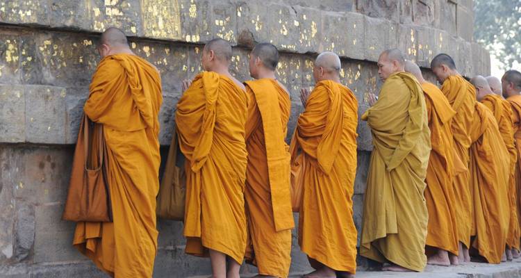 Rij van saffraangeel geklede boeddhistische monniken die bidden tegen een oude stenen stupa-muur verguld met bladgoud.