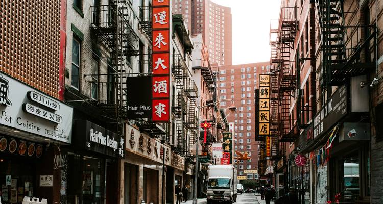 Ruelle étroite de Chinatown bordée d'enseignes commerciales bilingues, d'escaliers de secours et d'un camion de livraison sous une lumière du jour douce.