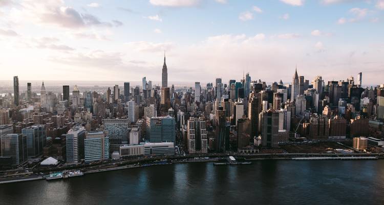 Vue aérienne panoramique de la ligne d'horizon de Manhattan s'étendant le long de l'East River sous un ciel d'après-midi lumineux.