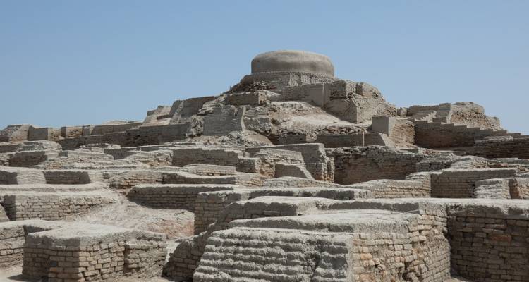 Estupa abovedada centrada sobre plataformas de ladrillo erosionadas bajo un cielo azul claro.