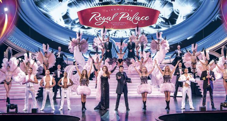 Une grande distribution d'artistes costumés pose sur une scène de cabaret vivement éclairée sous une enseigne Royal Palace.