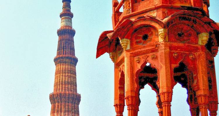 Ornate red sandstone minaret and pavilion of the Qutub Minar complex under a pale sky.