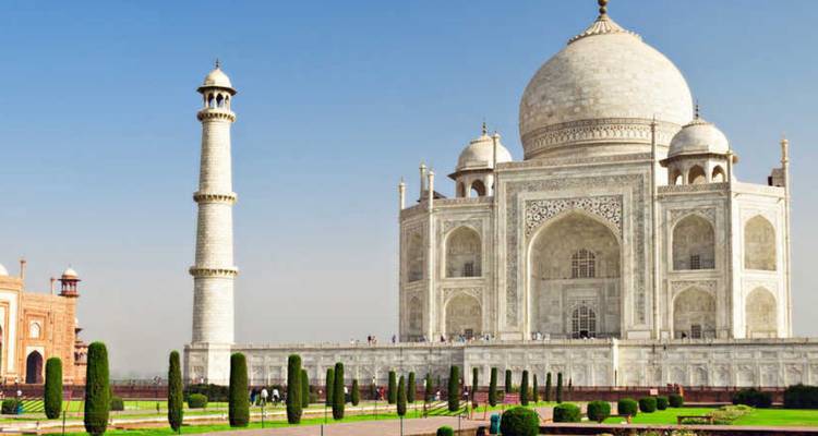 The white marble Taj Mahal with formal gardens under a clear blue sky.