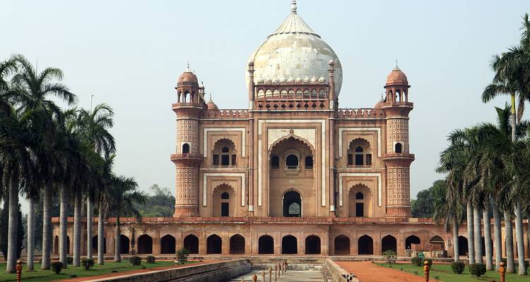 Safdarjung Tombe, een elegant Mughal zandsteen mausoleum met een centrale koepel en palmbomen omzoomde wandelweg onder een heldere hemel.