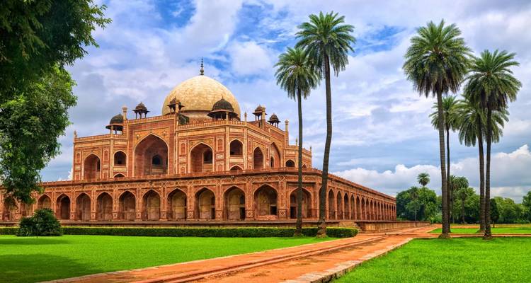 Humayun's Tombe, een grootse rode zandsteen Mogolmonument te midden van weelderige groene gazons en hoge palmbomen onder een heldere hemel.