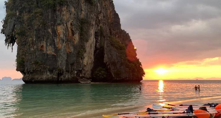 Dramatische kalkstenen klif die oprijst uit turkooizen zee bij zonsondergang met kajaks op een zandig strand getrokken.
