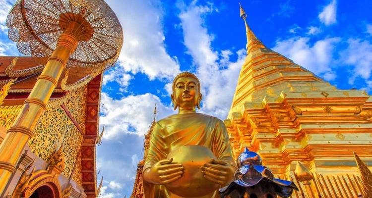 Gouden Boeddhabeeld en glanzende chedi van Wat Phra That Doi Suthep die straalt tegen een levendige blauwe hemel met wolken.