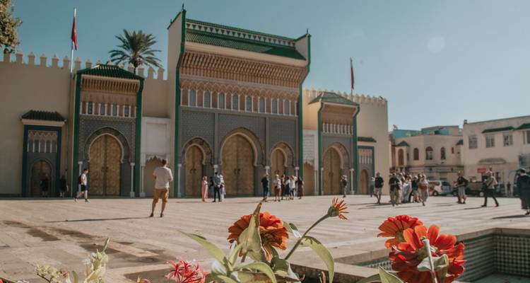 Royal Gate of Fes with tourists and foreground flowers on sunny day.