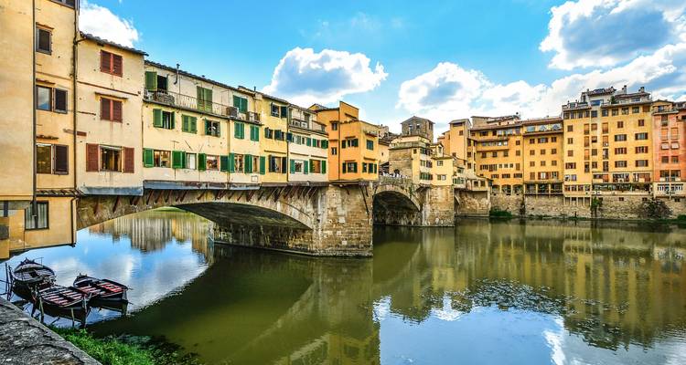 The historic Ponte Vecchio bridge spanning the Arno River with colorful buildings reflected in the water.