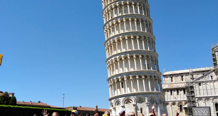 Tour group posing playfully in front of the Leaning Tower of Pisa on a sunny day.