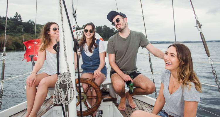 Vier vrienden lachen samen op het dek van een zeilboot op een rustige meer.