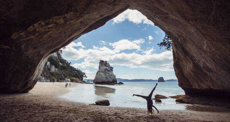 Bezoekers genieten van een zandige baai omlijst door een massieve rotsboog met turkooizen zee daarachter.