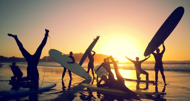 Surfers nemen speelse poses aan met hun planken tegen een levendige zonsondergang op nat zand.