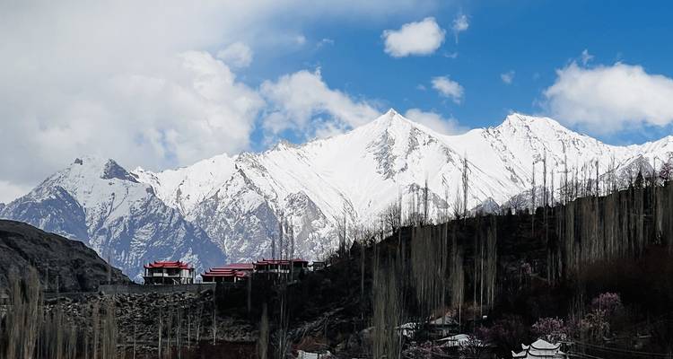 Cordillera con cumbres nevadas elevándose detrás de casas en la ladera con álamos altos
