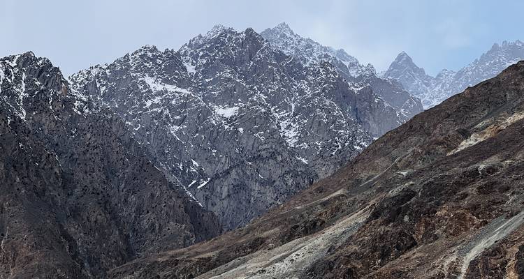 Caras montañosas escarpadas y dentadas espolvoreadas con nieve fresca bajo un cielo pálido