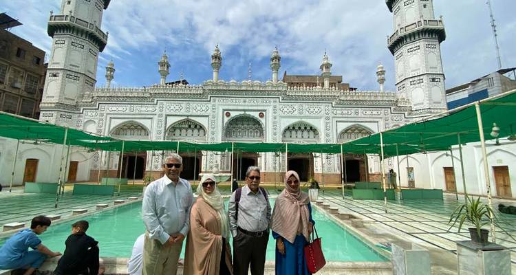 Visitantes de pie frente al patio de una mezquita blanca ornamentada con piscina turquesa