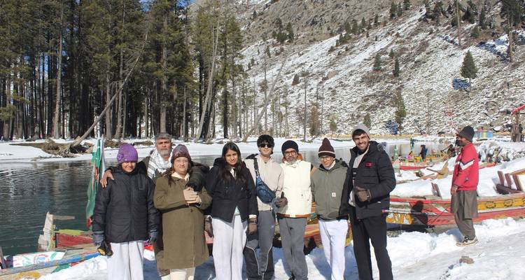 Grupo de viajeros de pie junto a botes coloridos en la orilla nevada del lago con pinos