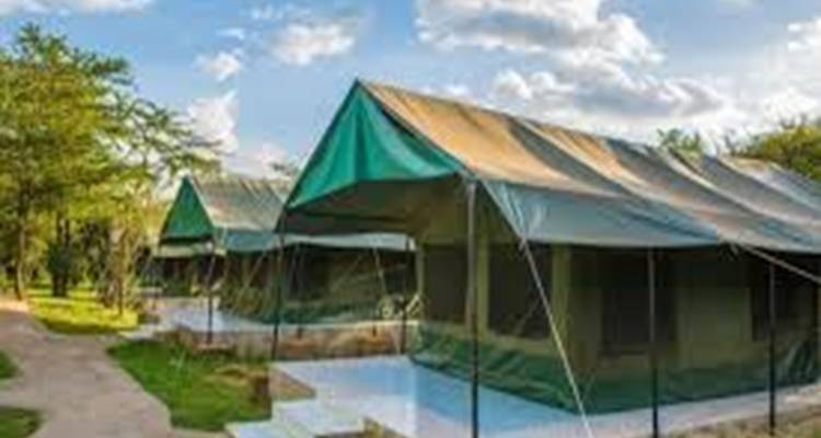 Low-resolution image of several green safari tents lined along a dirt path.
