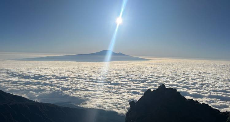Sol brillante sobre un manto de nubes con la silueta del Kilimanjaro en el horizonte.