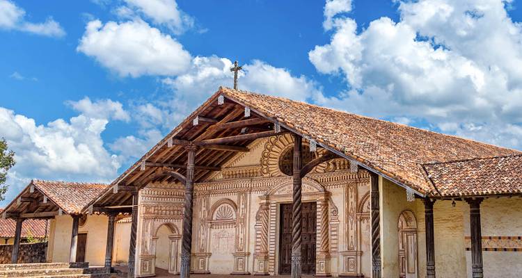 Well-preserved Jesuit mission church with ornate wooden façade under a bright blue sky and fluffy clouds.