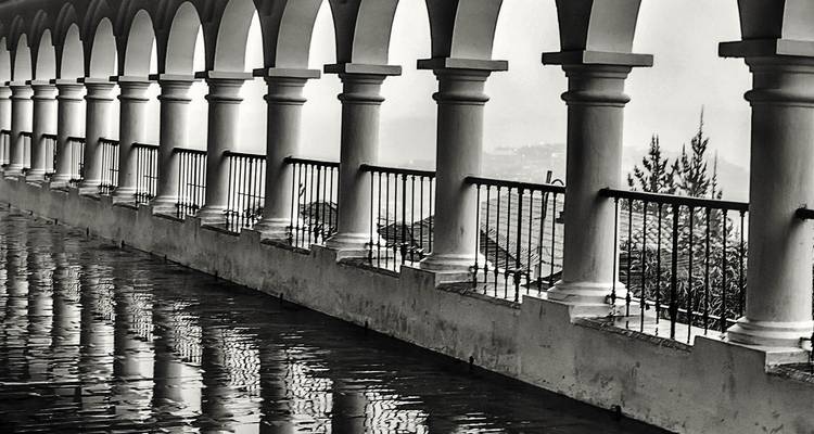 Black-and-white photo of wet tile floor reflecting a series of white arches and columns in Sucre.