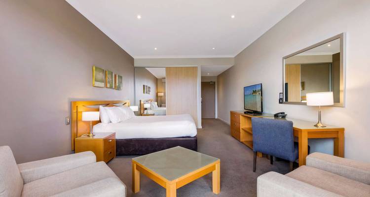 Modern, neutral-toned hotel room with king bed, lounge chairs, desk and flat-screen TV