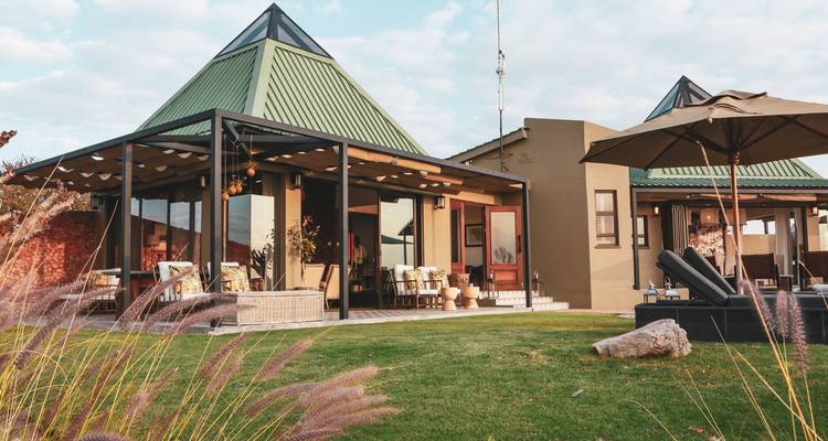 Modern chalet-style building with green roofs, patio furniture and manicured lawn under a bright sky.