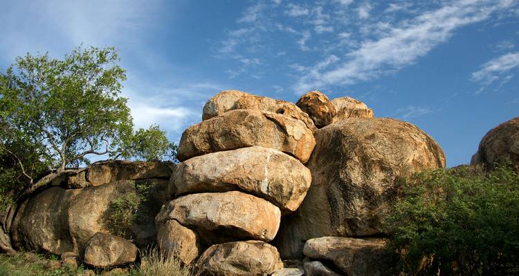 Stacked round granite boulders beside low bushes under a blue sky with wispy clouds.
