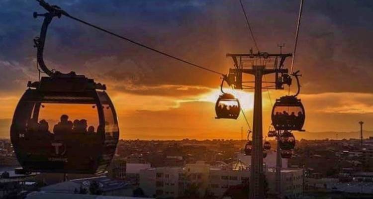 Silhouetted cable cars glide across an orange sunset sky above the city of La Paz.