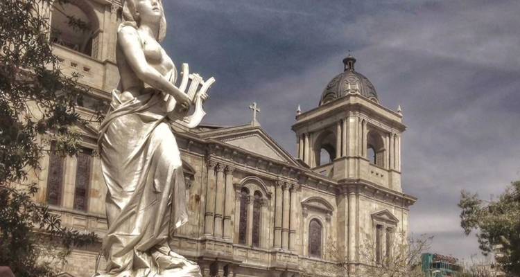 Marble statue in foreground with ornate cathedral façade behind under partly cloudy sky.