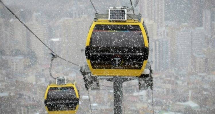 Yellow cable cars travel through falling snow over a blurred cityscape of La Paz.